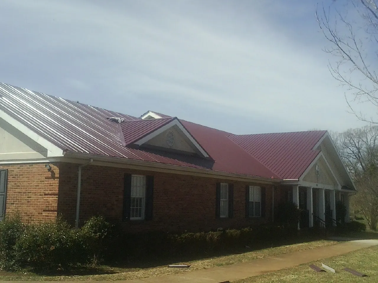 Red metal roof with gabled entries on a long brick building, from a Hail Damage Roof Repair job in Bradenton Beach