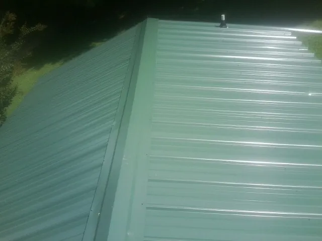 New green metal panels meeting at the ridge of a roof — Flat Roof Repair work by our crew in Bradenton Beach