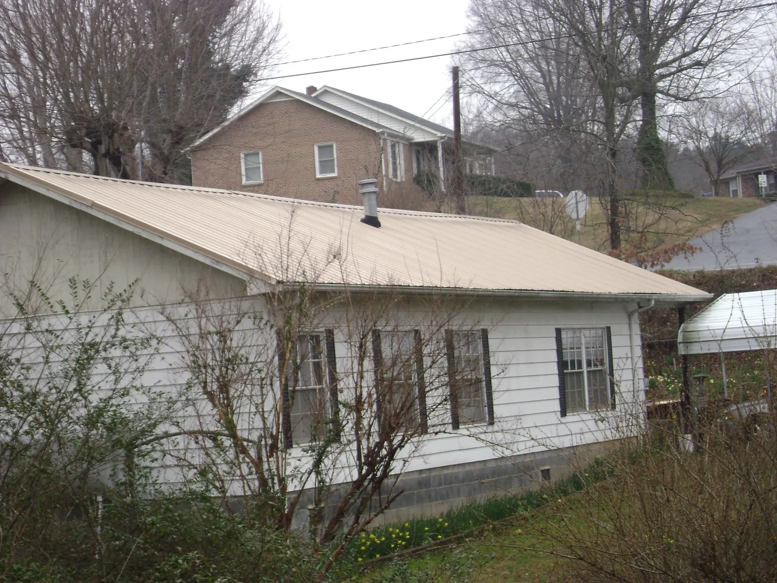 Tan metal roof on a white sided house set into a hillside — Commercial Roofing by Roofing Brothers in Bradenton Beach