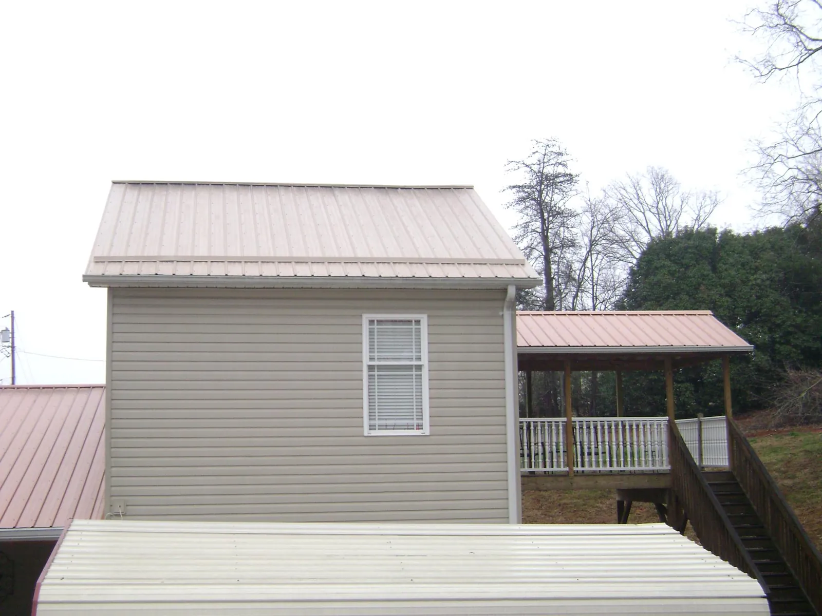 Tan metal roofs on a two story addition and attached porch, from a Roof Replacement job in Bradenton Beach